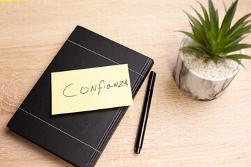 Notebook with confianza note, pen and plant on wooden desk