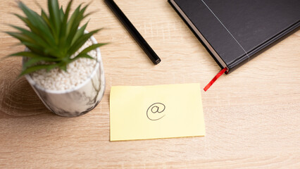 Email symbol on sticky note with pen and notebook on wooden desk