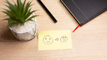 Sticky note showing happy face turning sad on office desk