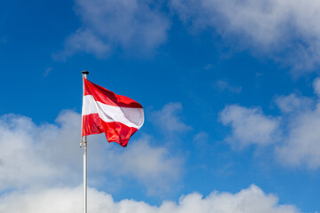 The Austrian red white red national flag flutters against a blue alpine sky