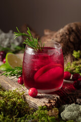 Cranberry cocktail with ice, lime, and rosemary on a old wooden board.