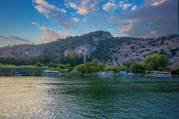 Fototapeta premium The rock-cut temple tombs of the ancient city of Kaunos in Dalyan, Muğla, Turkey. Beautiful view of Dalyan river with reed beds, excursion boats and carved tombs in the background.