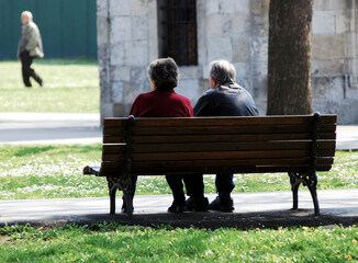 An elderly couple rests on a wooden bench
