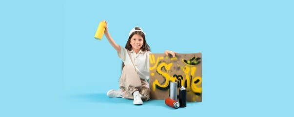 Little girl with spray cans and graffiti sitting on light blue background