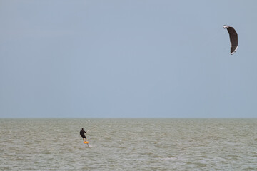 A man is riding a hydrofoil surf board with paraglide in sea