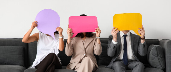 Business people with blank speech bubbles sitting on sofa in office
