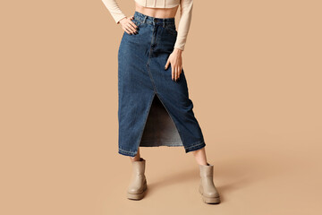 Naklejka premium Legs of beautiful young woman wearing blue long denim skirt on beige background