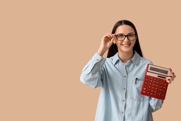 Happy young woman with calculator on brown background