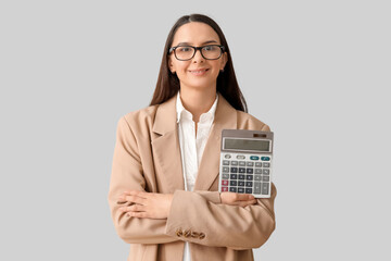 Beautiful young woman with calculator on grey background