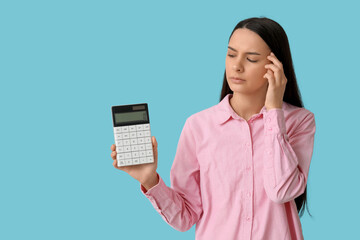 Thoughtful young woman with calculator on blue background