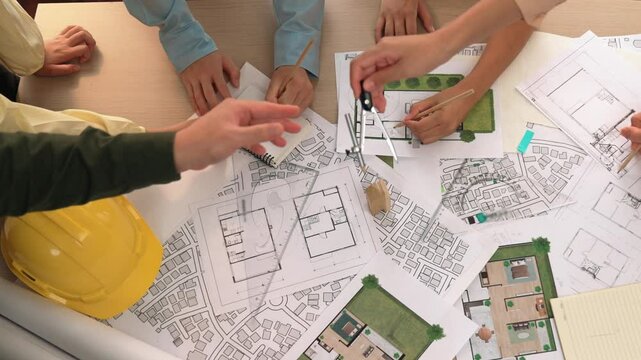 Architect and safety engineer discussion about building construction use blueprint on table with architectural document, measurement tool and wooden block scatter around at modern office. Delineation.