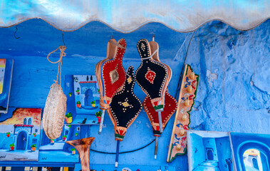 A blue wall with red and black leather bellows hanging, surrounded by local paintings and crafts,...