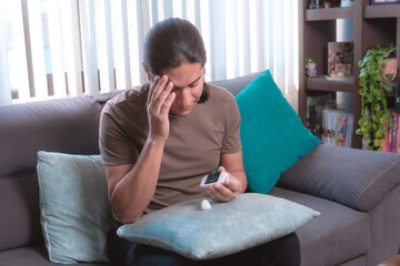 Middle-aged man measures his blood sugar level with a glucometer, he is sitting on the couch at home, home health.