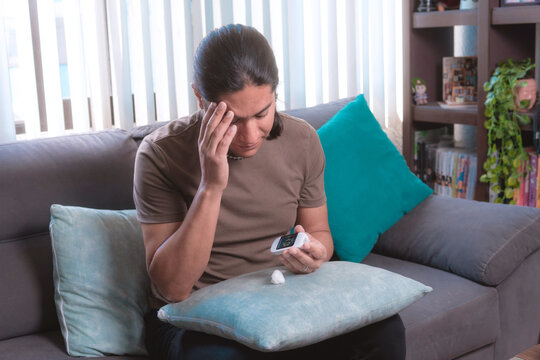 Middle-aged man measures his blood sugar level with a glucometer, he is sitting on the couch at home, home health.
