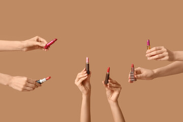 Female hands with many lipsticks on brown background