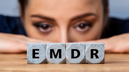 Eye Movement Desensitization and Reprocessing Psychotherapy Treatment concept. Letters EMDR written on grey cubes. Woman's face with a focused look behind. 