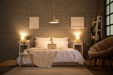 Interior of bedroom with cozy blanket on bed and glowing lamp late in evening