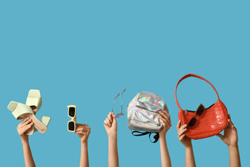 Female hands with stylish sunglasses, different bags and sandals on blue background