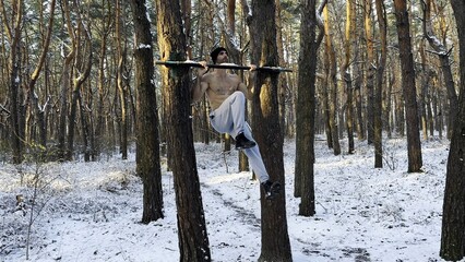 Athletic man doing static exercises on horizontal bar at forest. Sportive guy training abdominal...