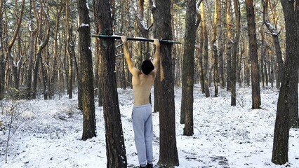 Athletic guy doing pull ups at beautiful forest. Strong and muscular man exercising on horizontal...