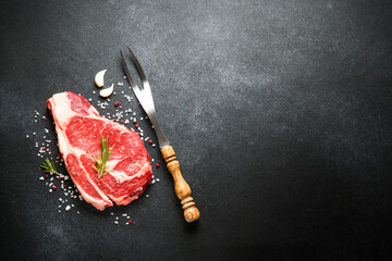 Raw meat steak. Beef steak and fork with spices on black background. Top view with copy space.
