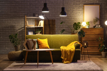 Sofa, coffee table with wooden hand, books and glowing lamps in interior of living room