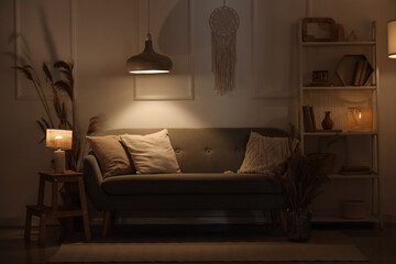 Interior of living room with cozy sofa, pampas grass, shelving unit and glowing lamps