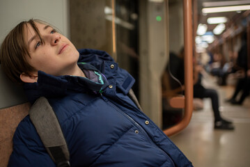 boy in a blue winter jacket sits in a subway train carriage	