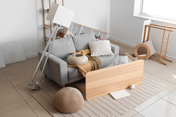 Interior of messy living room with grey sofa and overturned furniture after earthquake