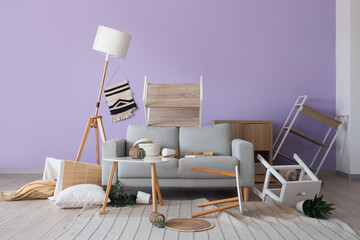 Interior of messy living room with grey sofa and overturned furniture after earthquake