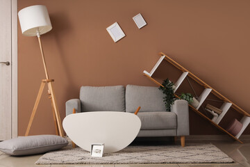 Interior of messy living room with grey sofa and overturned furniture after earthquake