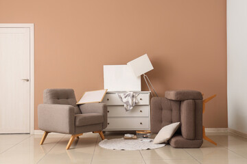 Interior of messy room with armchairs and overturned furniture after earthquake near beige wall