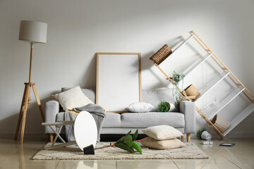 Interior of messy room with grey sofa and overturned furniture after earthquake