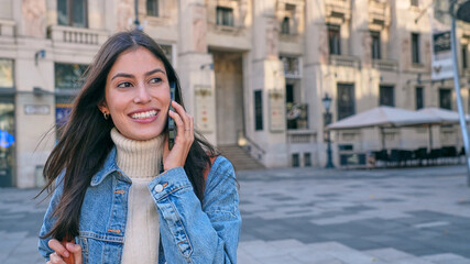 Beautiful Latin smiling woman talking on the phone while walking in the city. Tourist and people...