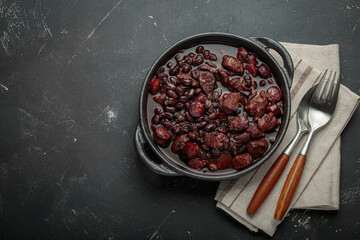 Feijoada, a traditional brazilian stew in a cast iron pot,, ready to be served with a spoon and...