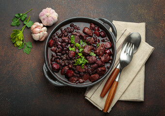 Brazilian feijoada, a hearty stew of black beans, various cuts of meat, and sausage, garnished with...