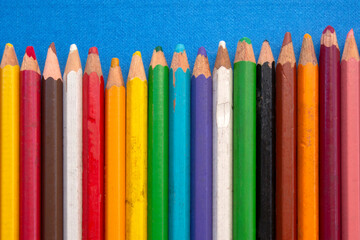 close up of colored wooden pencils in a row, on blue background. top view
