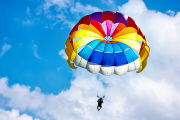 Paragliding using a parachute on background of blue cloudy sky.