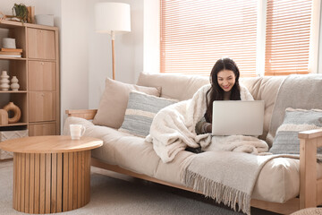 Young woman with warm plaid using laptop at home on winter day