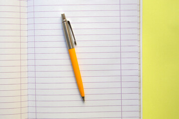 open notebook, with a pen on , on yellow background. top view