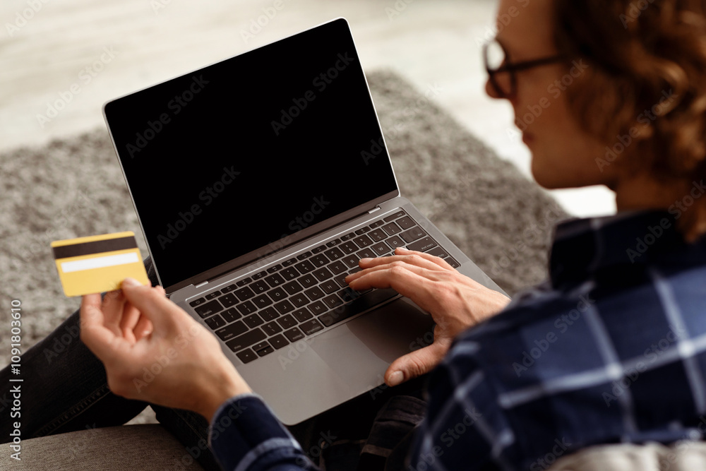 Poster Back-View Of Man Using Laptop And Credit Card Shopping Online On Computer With Empty Screen Sitting At Home. Guy Purchasing And Paying In Internet Store. Cropped, Selective Focus, Mockup