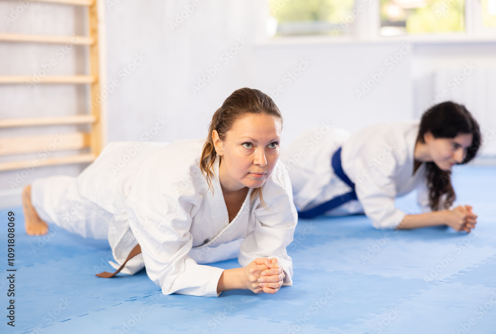 Wall mural Adult woman and young female karateka train their abs in studio