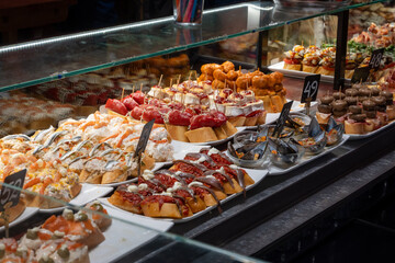 Typical snacks of Basque Country, variety of pinchos or pinxtos oven baked sea food, bread, skewers with jamon, goat cheese served in bar in San-Sebastian or Bilbao, Spain, close up