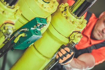 Worker Using Wrench on Hydraulic Machinery in Industrial Facility During Daytime