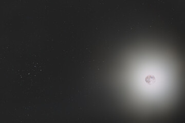 The super mineral Moon in its full phase, in conjunction with the Pleiades (or Messier 45) in the Taurusc constellation and some stars on background. You can see the lunar glow so bright.