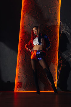 Woman at halloween as Harley Quinn party stay near wall with backlight
