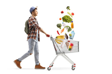 Full length profile shot of a male student pushing a shopping cart and collecting falling groceries