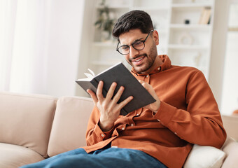 Portrait of young Middle Eastern man wearing eyeglasses holding paper book or diary, sitting on...
