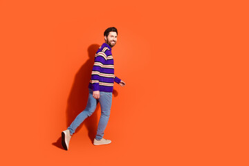 Confident man in a striped sweater walking against vibrant orange background, expressing joy and movement