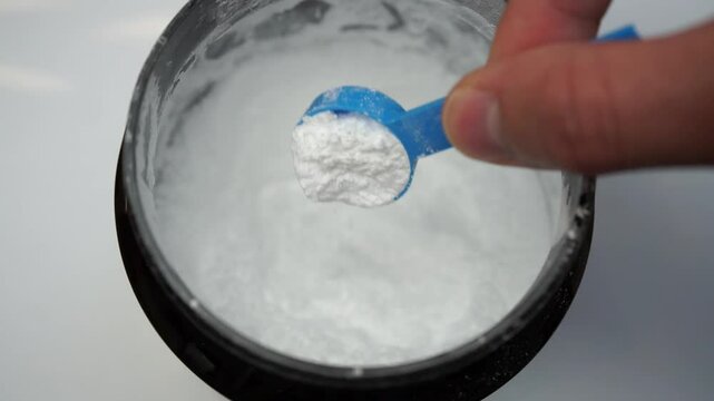 Close up of a hand scooping creatine with a scoop